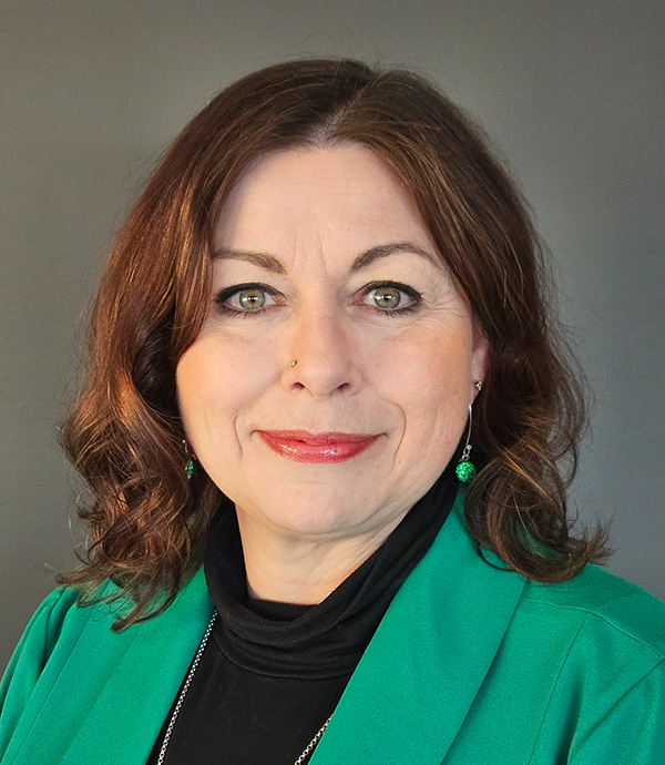 A woman with shoulder-length dark red hair and wearing a green blazer smiles.
